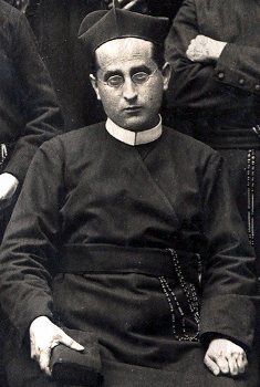 Fr Donato Jiménez seated, wearing a biretta and holding a book, in a group photograph from 1915.
